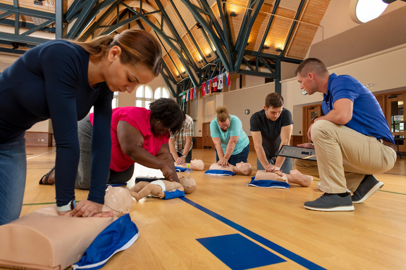 Group of people participating in a CPR training session in a gymnasium.